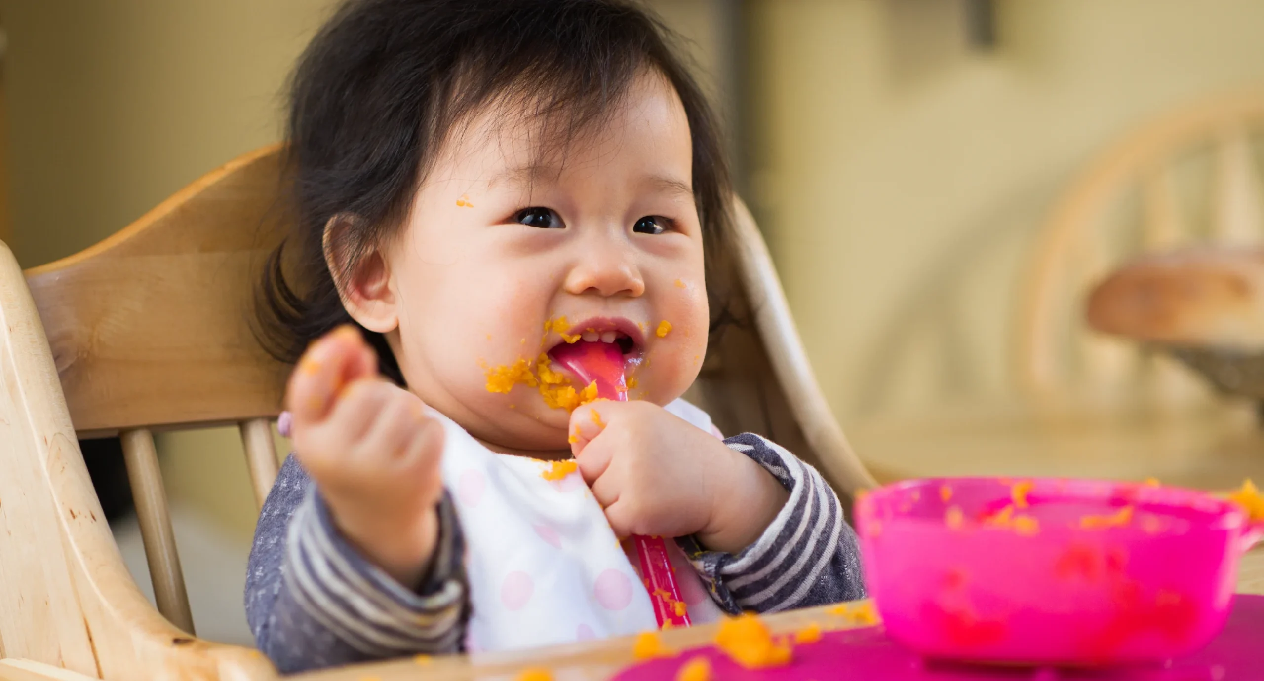 baby in high chair eating mashed sweet potato