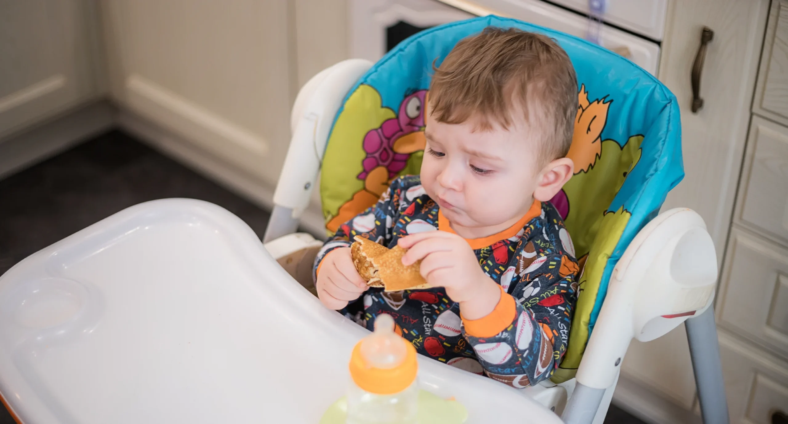 10 month old baby sitting in high chair holding healthy looking pancake