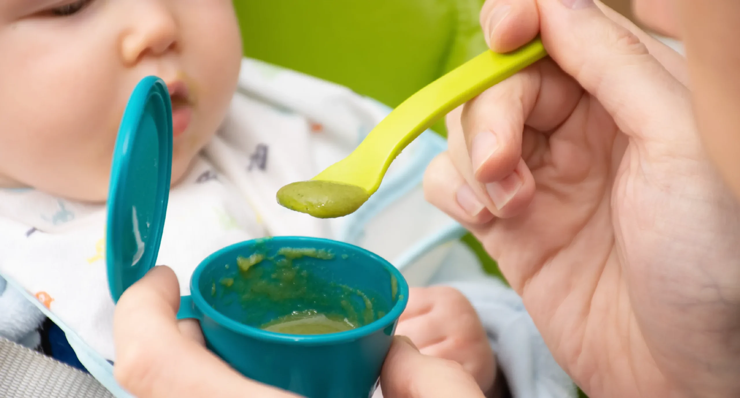parent feeding baby a green smooth puree